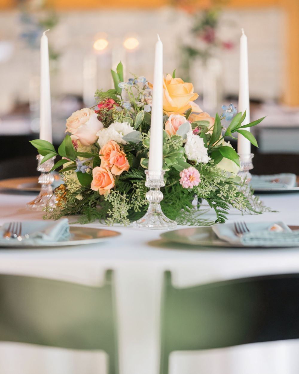 Wedding reception centerpiece with peach roses, white candles, and lush greenery on white table.bell manor Chillicothe ohio