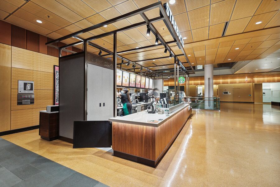 Modern cafeteria serving counter with wood paneling, track lighting, and open kitchen in a bright commercial space.