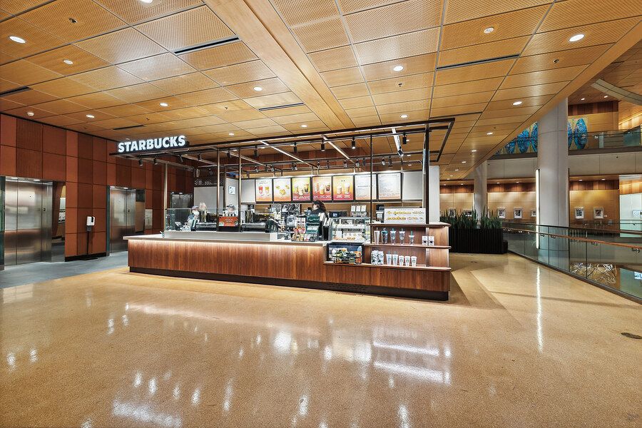 Modern Starbucks coffee kiosk in a spacious building lobby with wood paneling and polished floors.