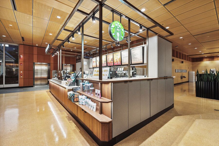Modern Starbucks coffee kiosk with wood paneling, menu boards, and open counter in a spacious lobby interior.
