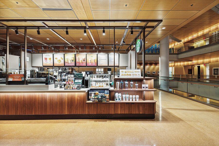 Modern Starbucks coffee shop interior with wooden counter, menu boards, and open atrium in a shopping mall.