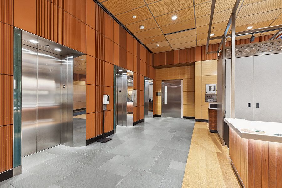 Modern office building lobby featuring sleek wood-paneled elevator banks with stainless steel doors and slate tile flooring.