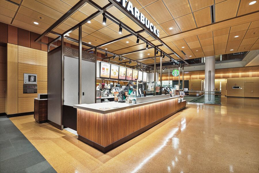 Modern Starbucks coffee kiosk with warm wood counter in a spacious open lobby with polished floors.