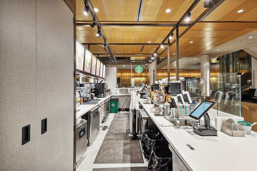 Starbucks café interior showing espresso equipment, POS terminals, and wood ceiling panels.