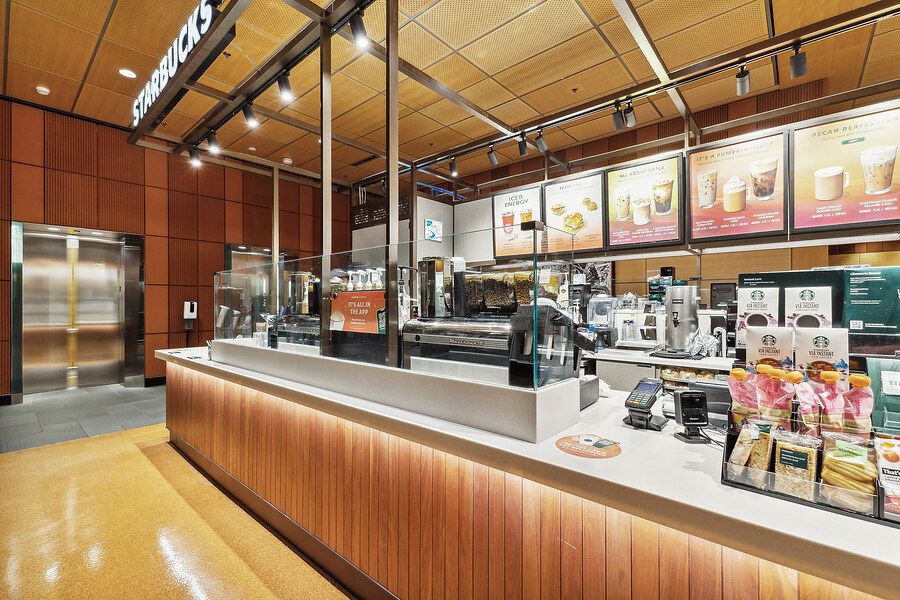 Modern Starbucks coffee shop interior with wooden counter, espresso machines, and illuminated menu boards.