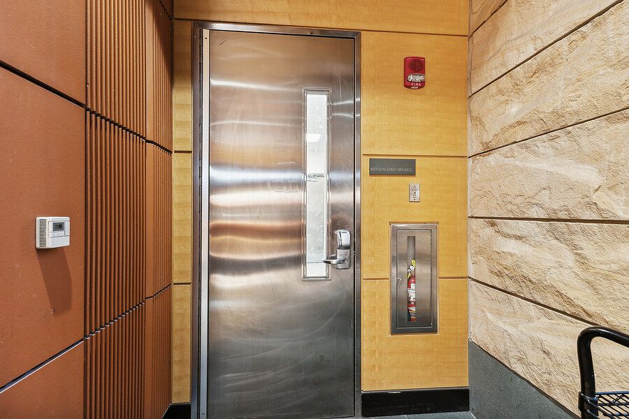 Stainless steel elevator door with modern wood and stone wall panels in a contemporary building lobby.