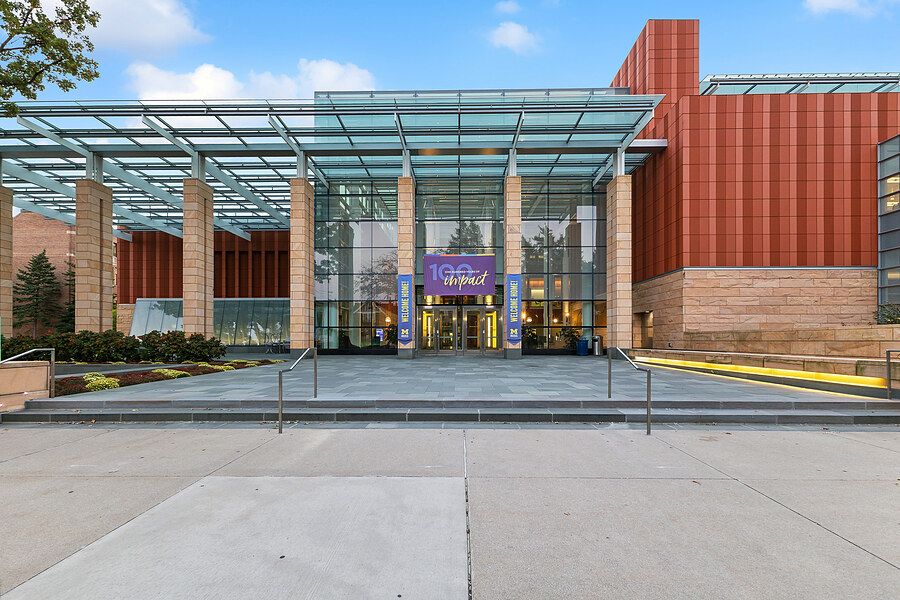 Modern hotel entrance with glass canopy, brick facade, and wide accessible walkway under blue skies.