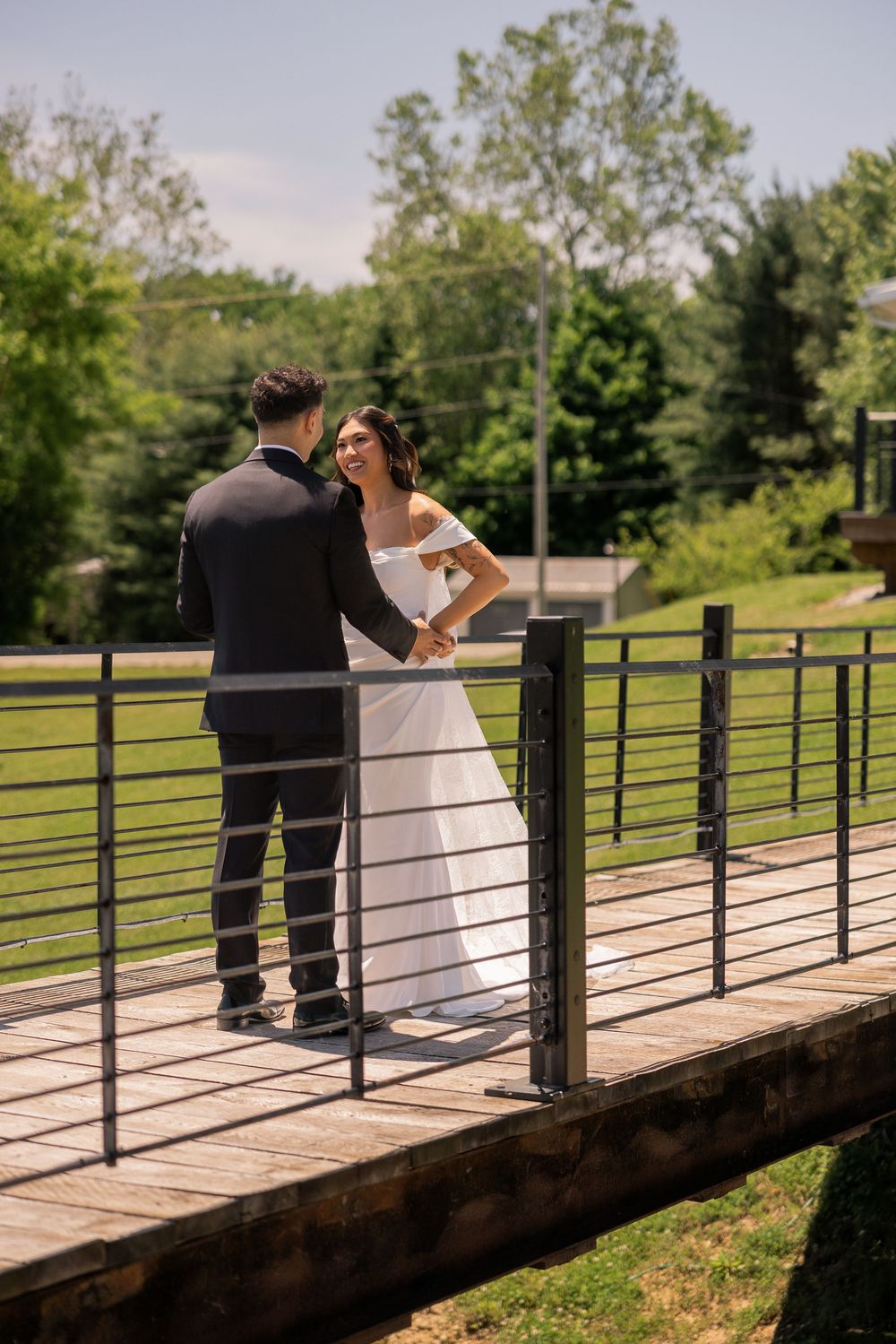 Bride and groom share a joyful moment on a wooden bridge surrounded by lush greenery on their wedding day.