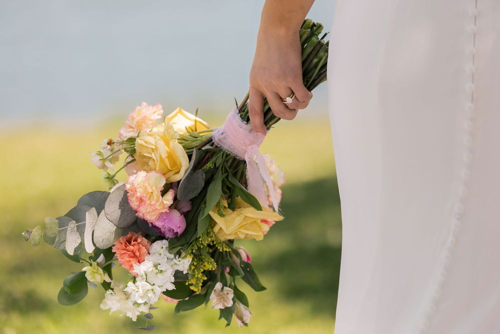 Bride holding a colorful wedding bouquet with pink, yellow, and white flowers outdoors.