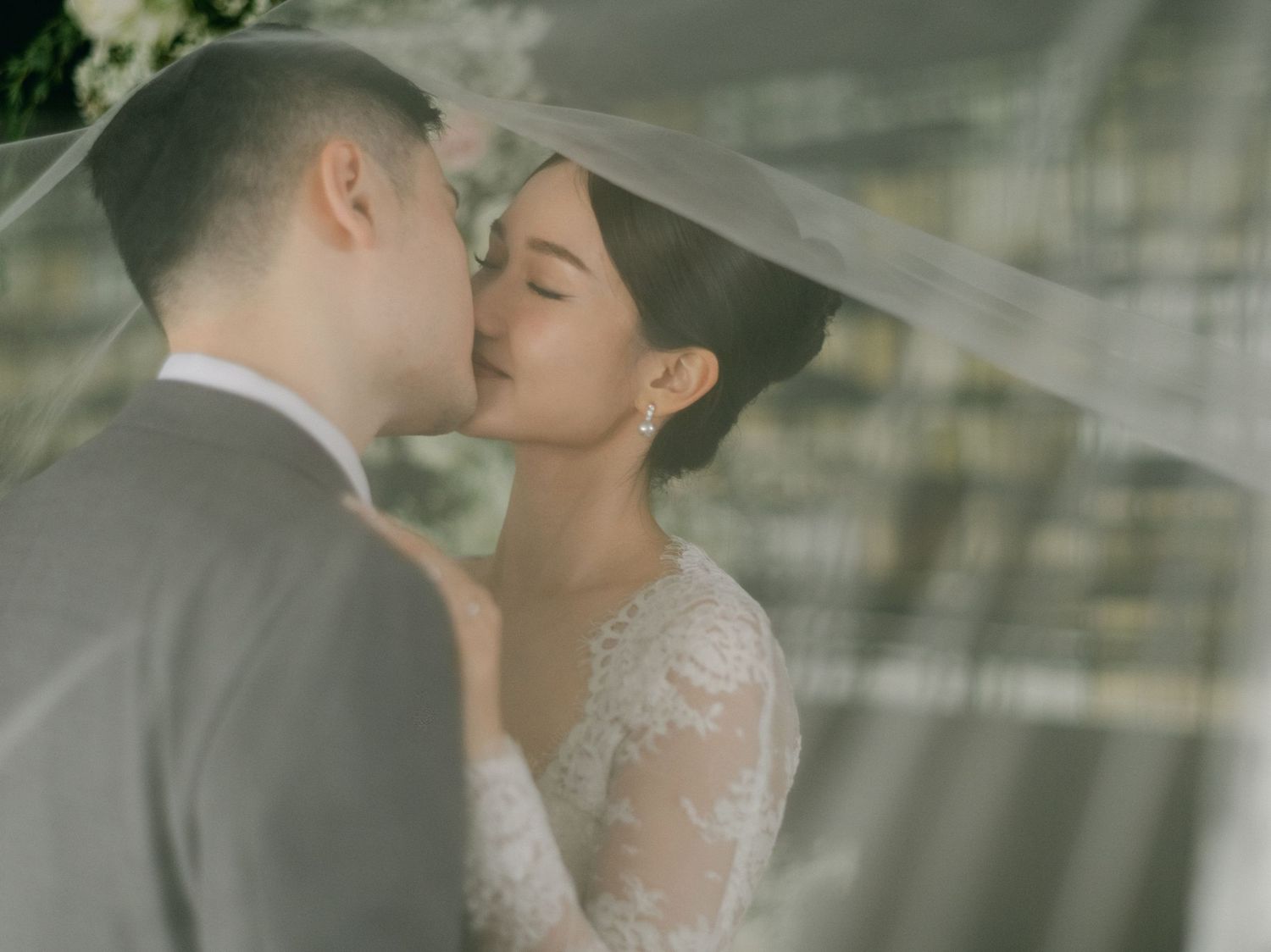 A bride and groom share a romantic kiss under a flowing white veil on their wedding day.