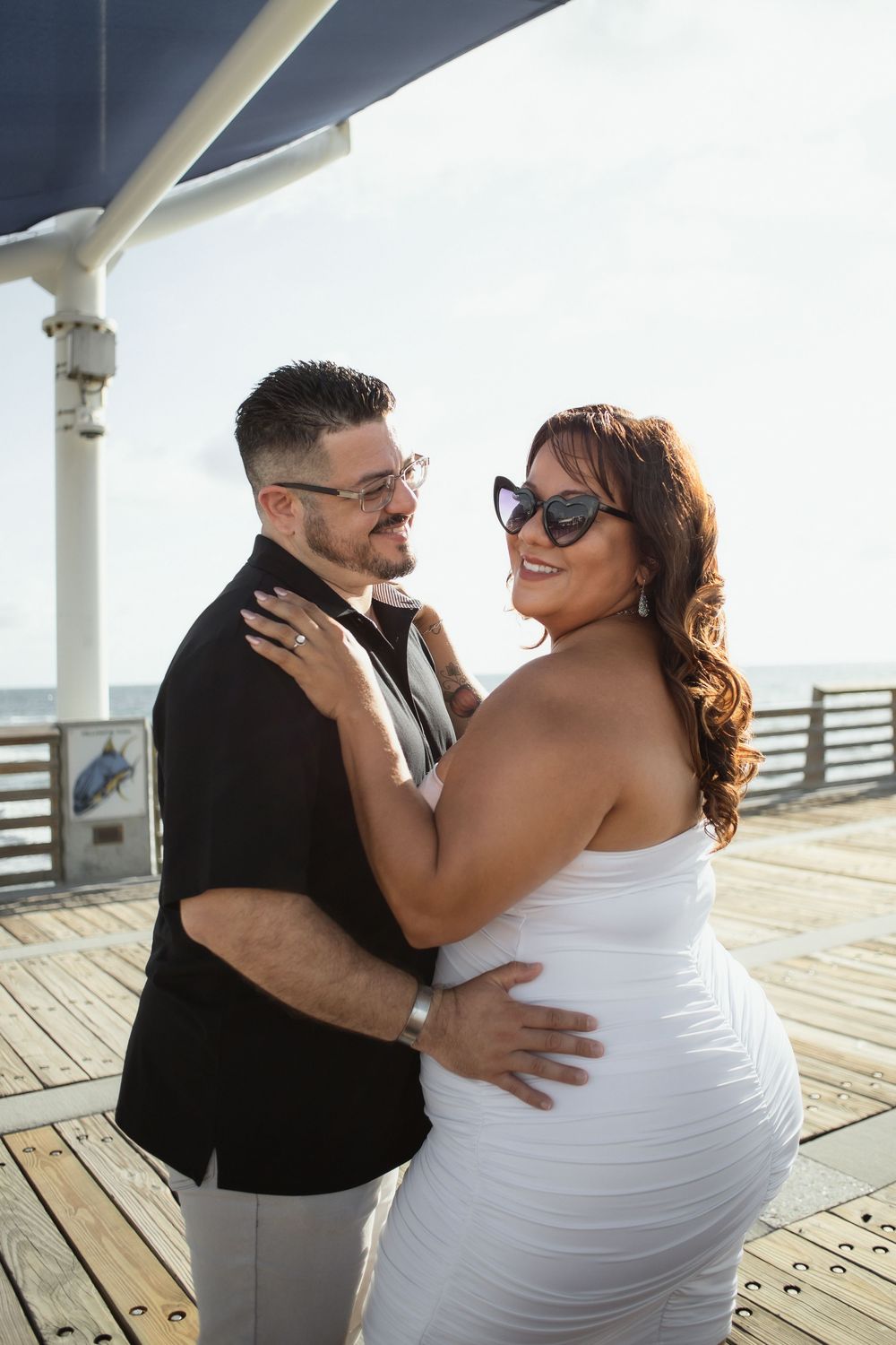 Couple embracing at Pompano Beach Pier during engagement couples session.