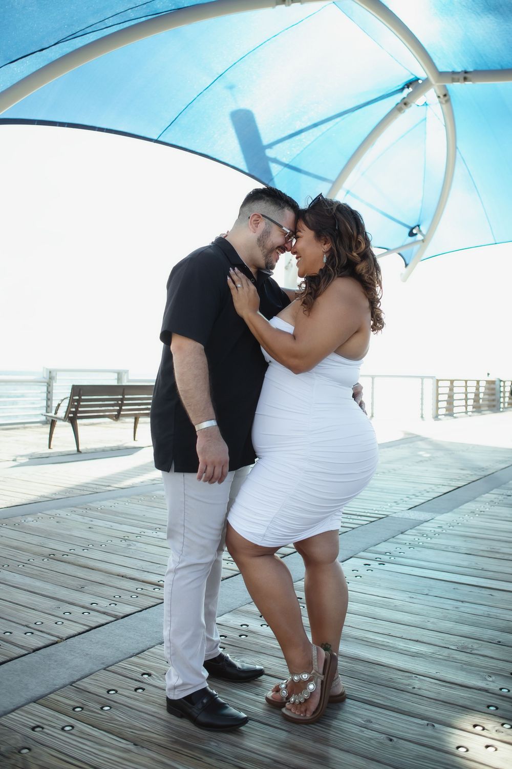Couple kissing at Pompano Beach Pier during engagement couples session.