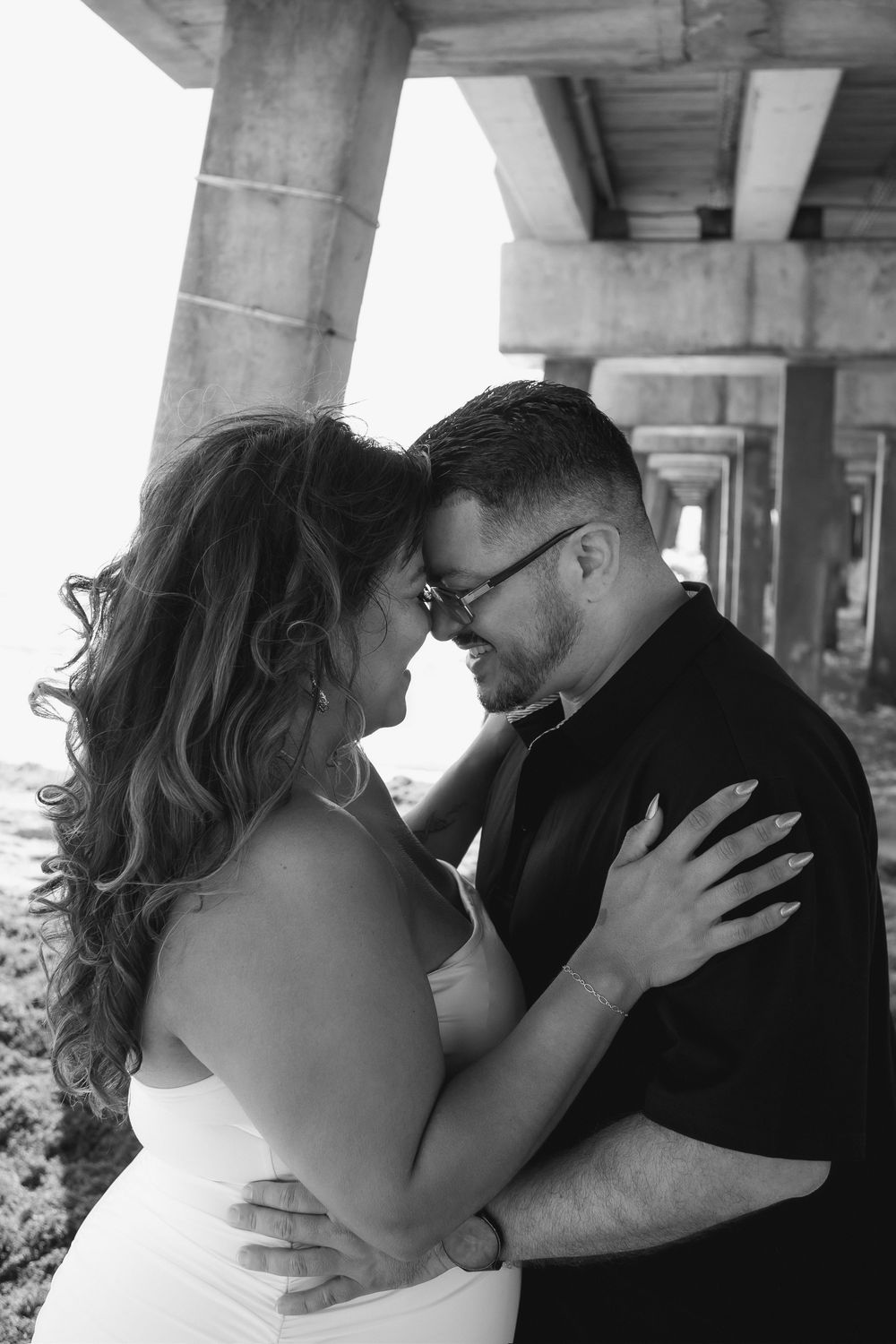 Couple kissing under Pompano Beach Pier during engagement couples session.