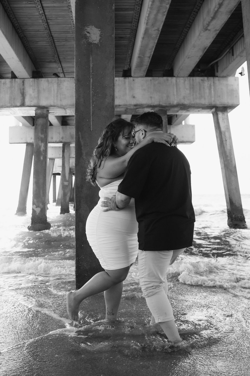 Couple kissing under Pompano Beach Pier during engagement couples session.