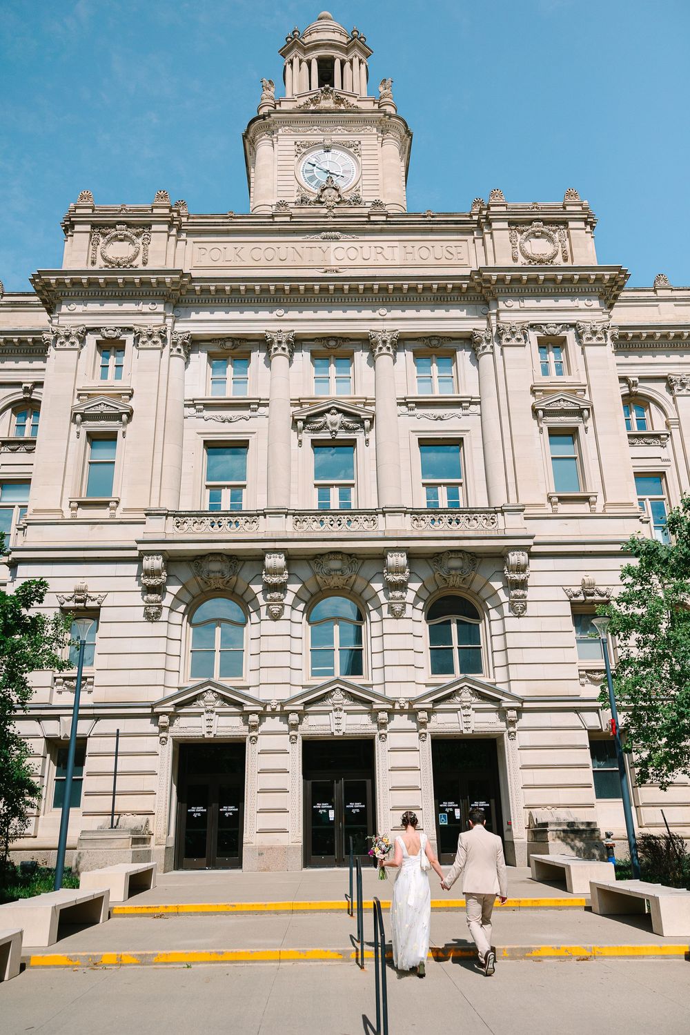 A couple walk hand-in-hand into the Polk County Courthouse in Des Moines on a sunny day.