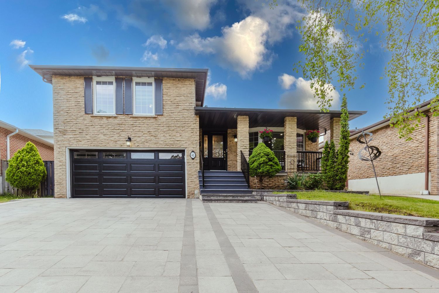 Two-story brick home with dark garage door, paved driveway, manicured landscaping, and modern curb appeal under blue sky.