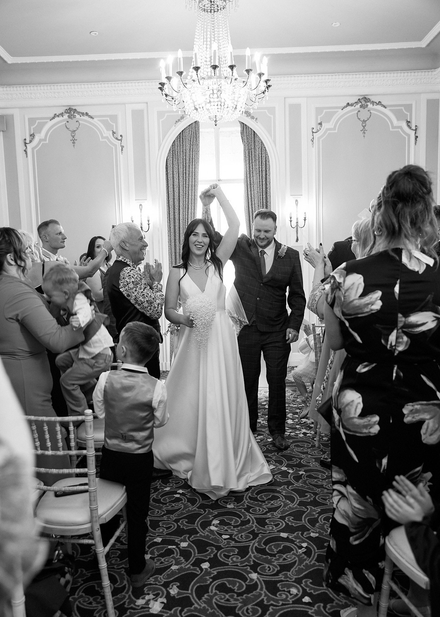 Black and white photo of bride and groom joyfully walking down the aisle after their ceremony.