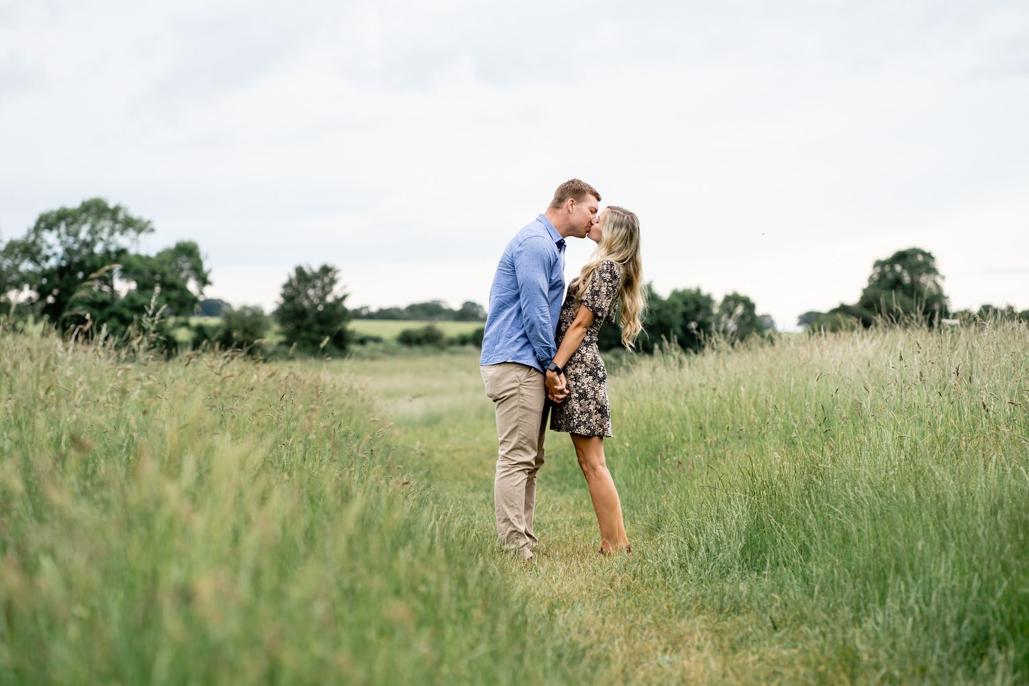Couple sharing a romantic kiss in a lush green meadow field on a cloudy day.