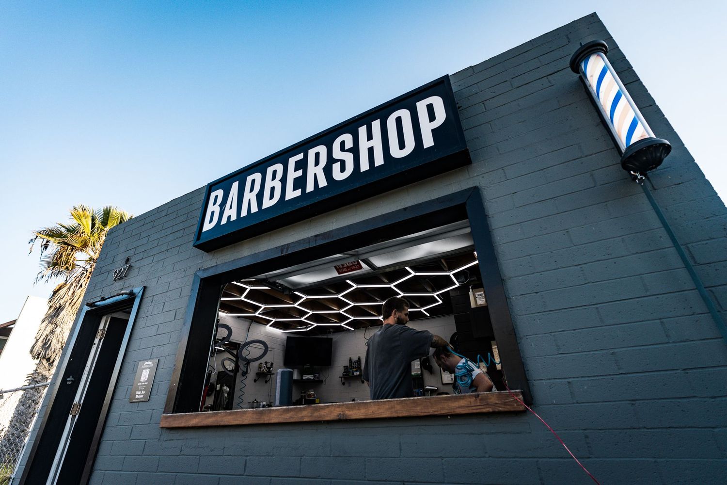 San Diego commercial photography of a modern barbershop exterior with a spinning pole, black brick storefront, and open service window.