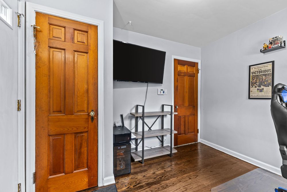 Bedroom with hardwood floors, two wooden doors, wall-mounted TV, and metal shelving unit.