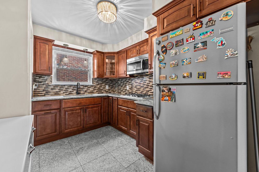 Classic kitchen with rich brown cabinets, mosaic tile backsplash, stainless appliances, and tile floor.