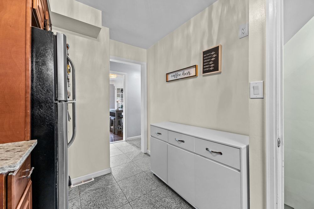 Narrow kitchen hallway with black stainless fridge, white cabinet, and neutral tile flooring.