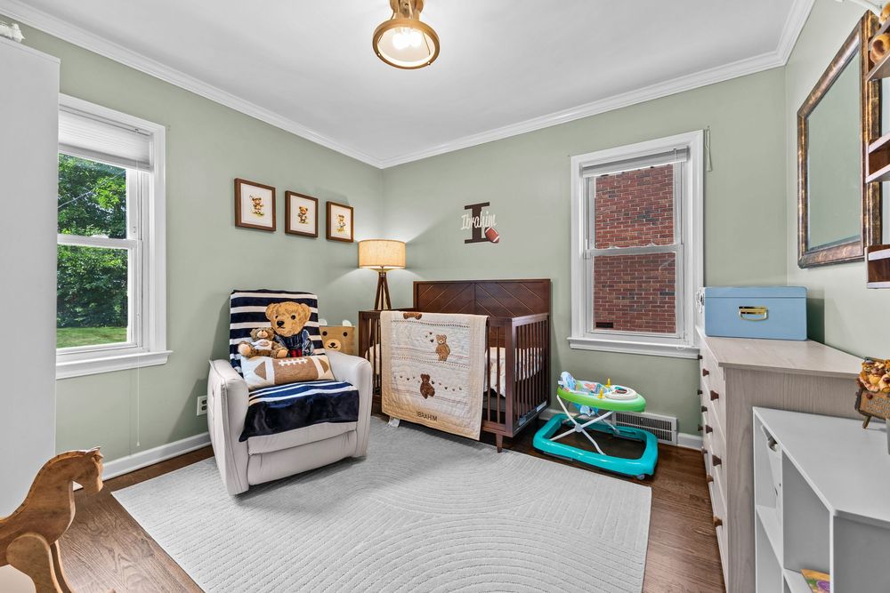 Cozy nursery with dark wood crib, crown molding, hardwood floors, and natural window light.