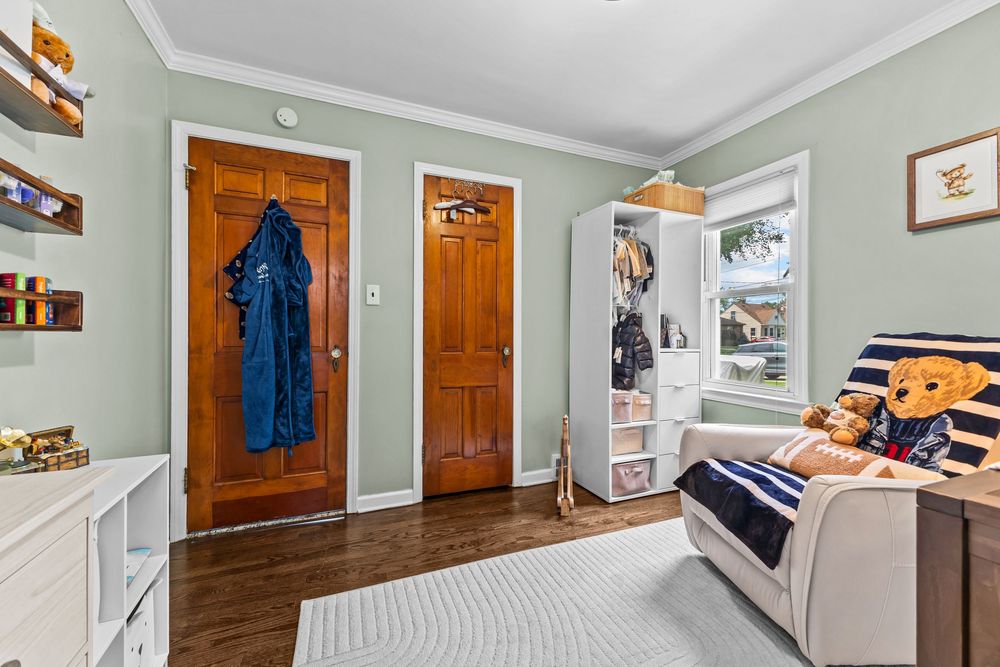 Small bedroom with hardwood floors, crown molding, wooden doors, and built-in shelving unit.