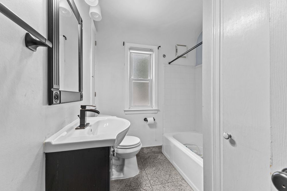 Clean white bathroom with dark vanity, pedestal sink, toilet, and shower-tub combo.