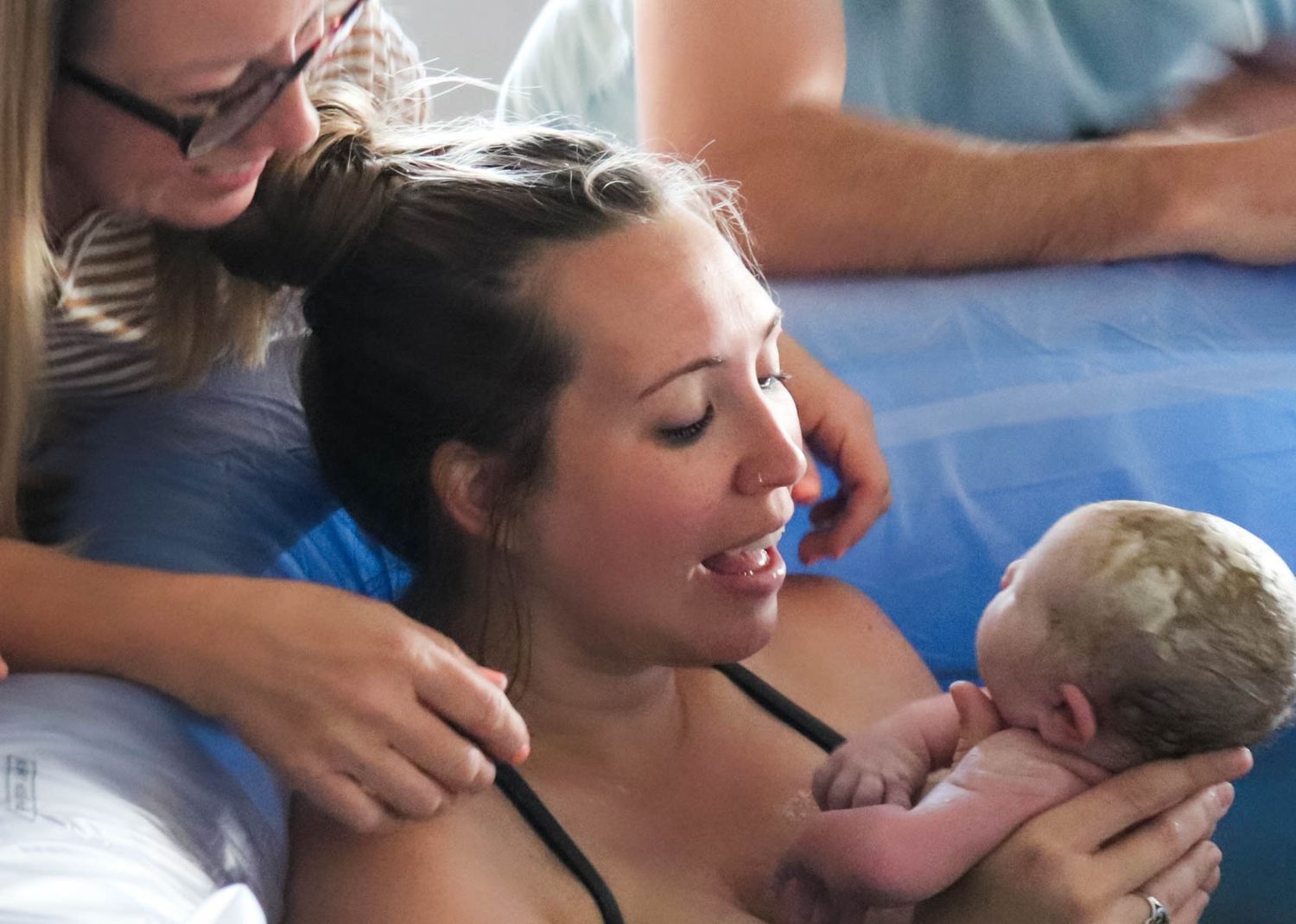New mother smiling while holding her newborn baby skin-to-skin after delivery.