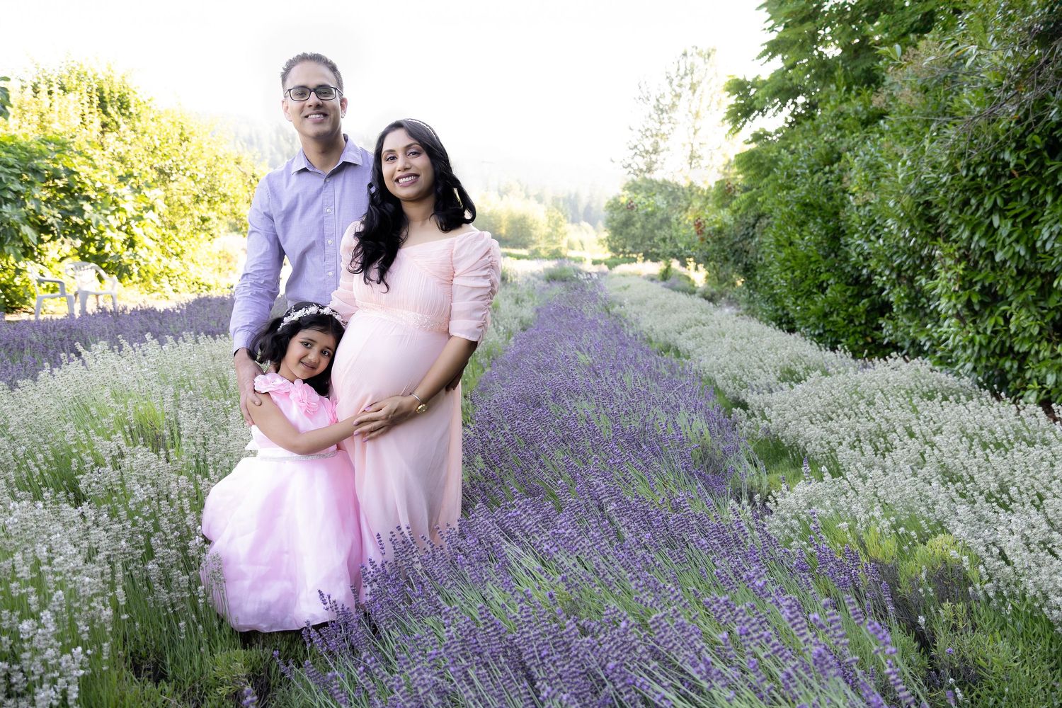 Pregnant woman in pink gown with husband and daughter in lavender field for maternity photo session.