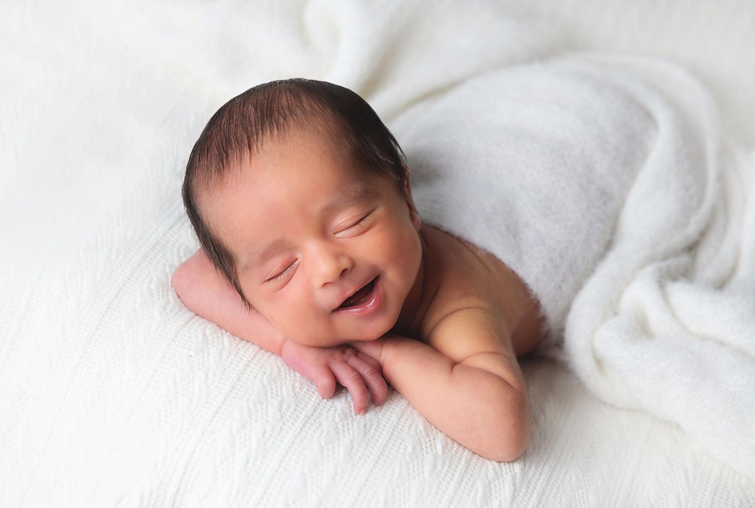 Smiling newborn baby peacefully resting on soft white blanket during professional photo session. During a photoshoot in Sidcup, Bexley
