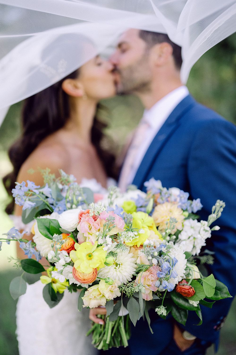 A romantic wedding moment under a flowing veil with a colorful bouquet in foreground.