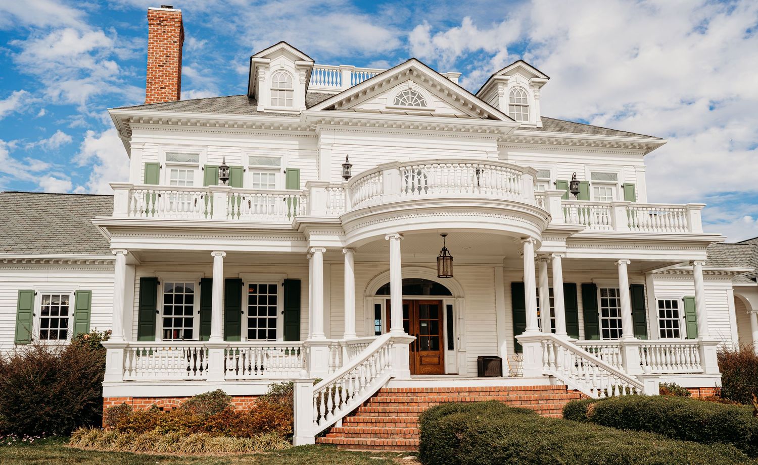 Elegant white colonial mansion with grand columns and wrap-around porches featuring classic Southern architecture.