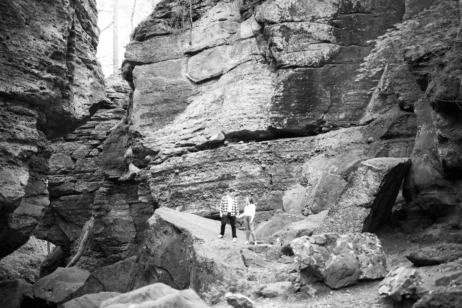 A person poses in a natural canyon formation surrounded by towering rock walls in black and white photography.