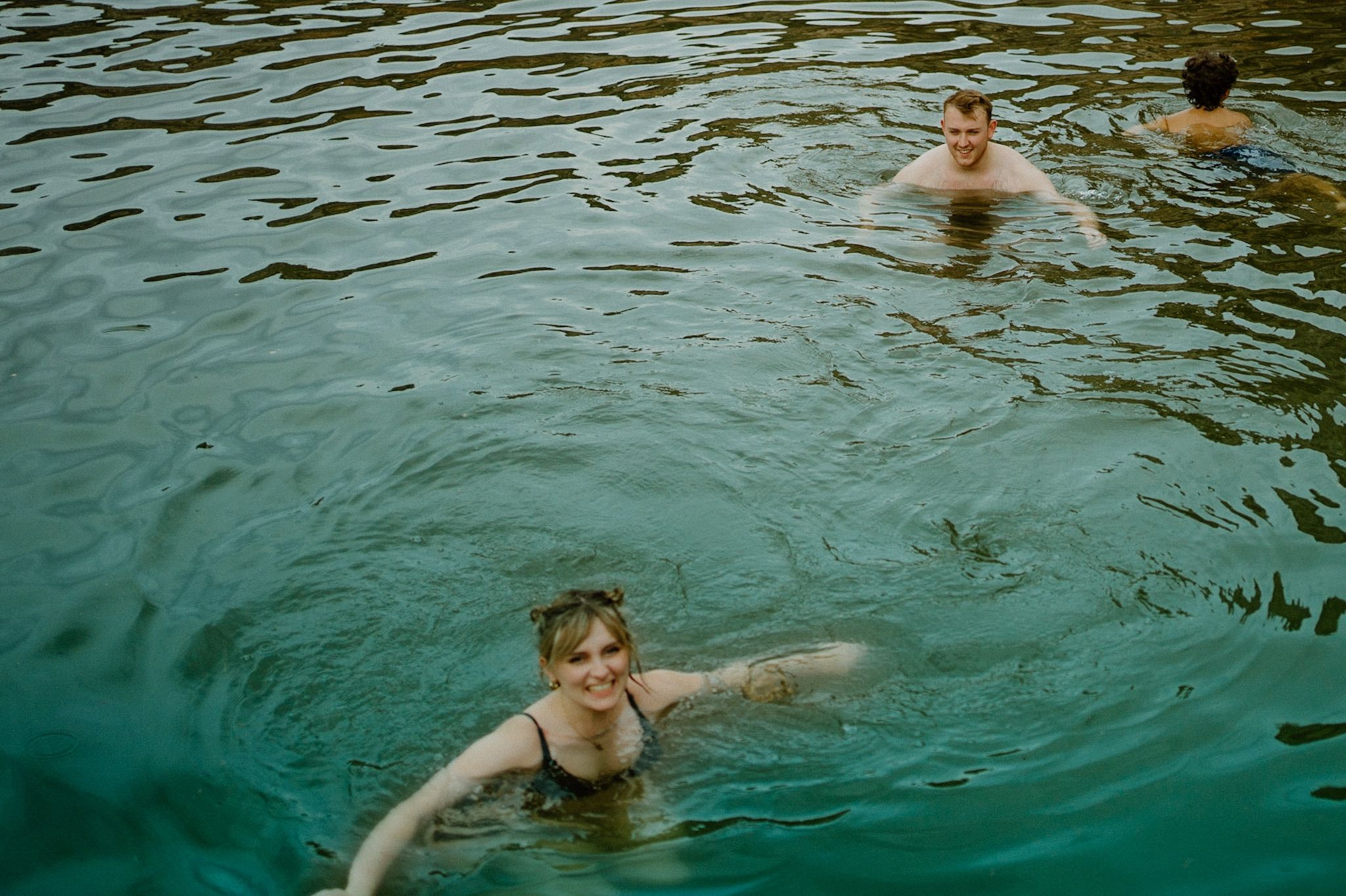 Someone swimming in turquoise rippling water on a sunny day, creating concentric circles in the natural pool.