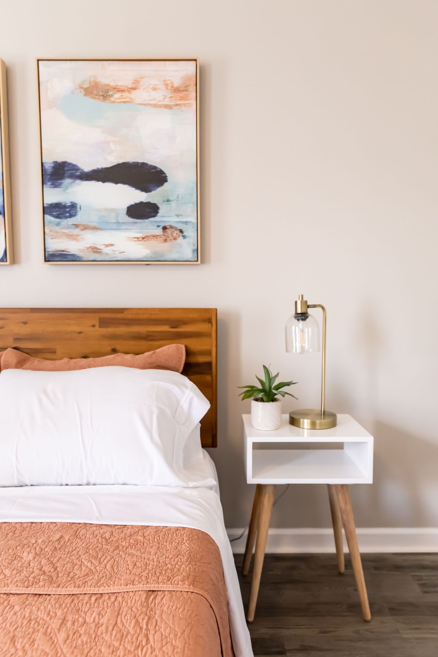 Minimalist bedroom with abstract art, wooden headboard, and coral bedding.