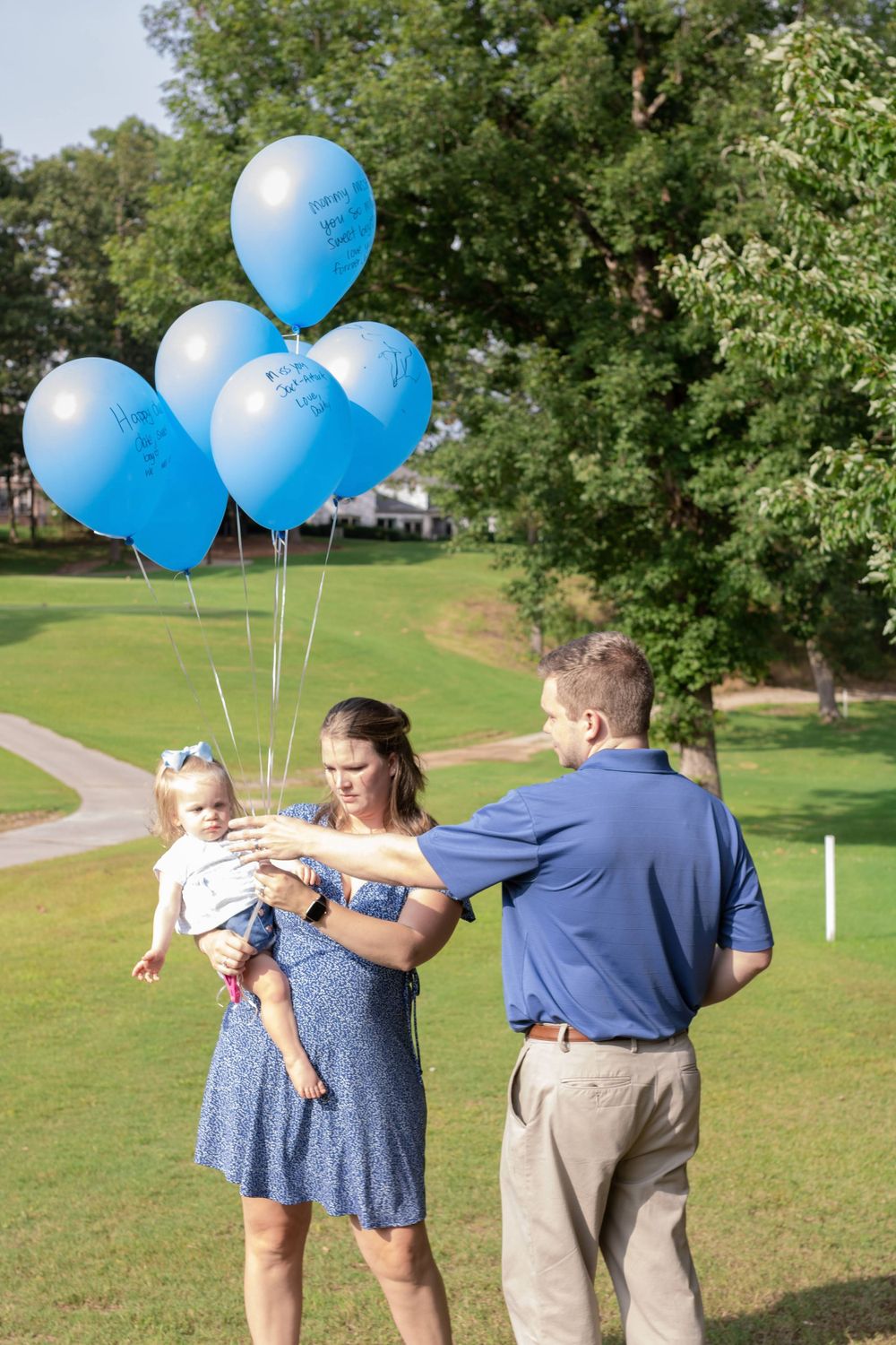 Light blue balloons float above a family enjoying a sunny afternoon in a grassy park setting.