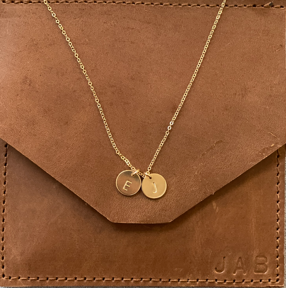 Gold chain necklace with two small circular pendant charms displayed on brown leather envelope.