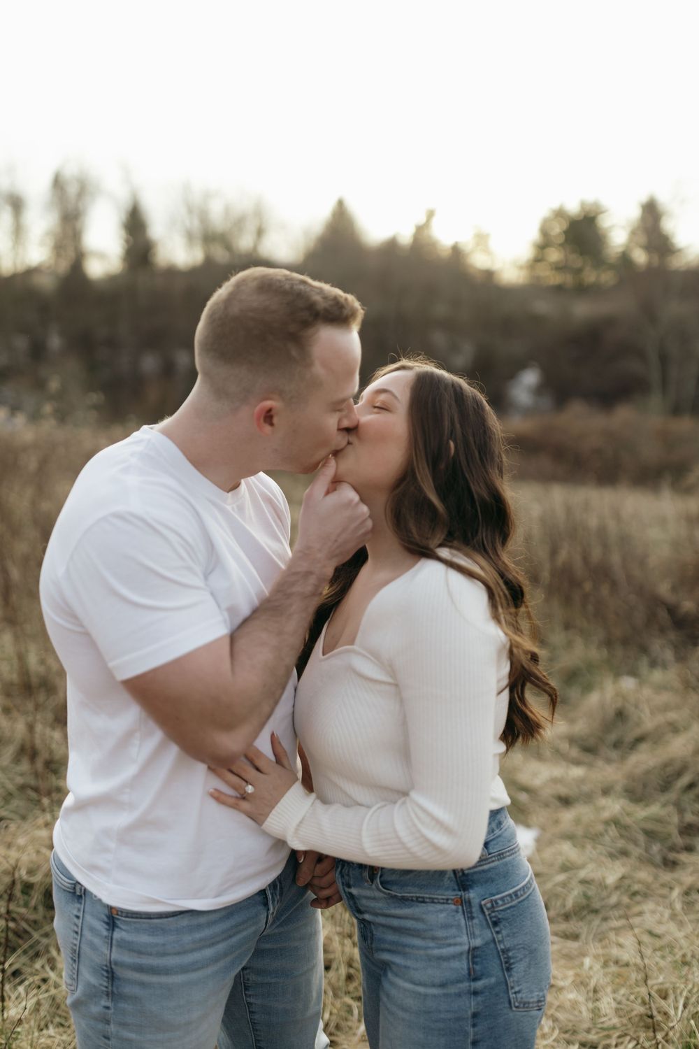 Intimate moment between couple sharing a tender kiss in field during golden hour.