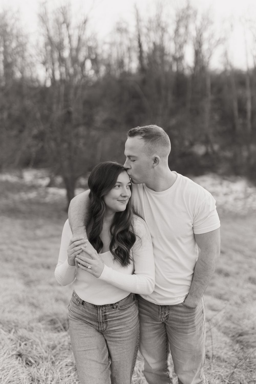 Romantic couple in casual attire share an intimate moment in a natural outdoor setting.