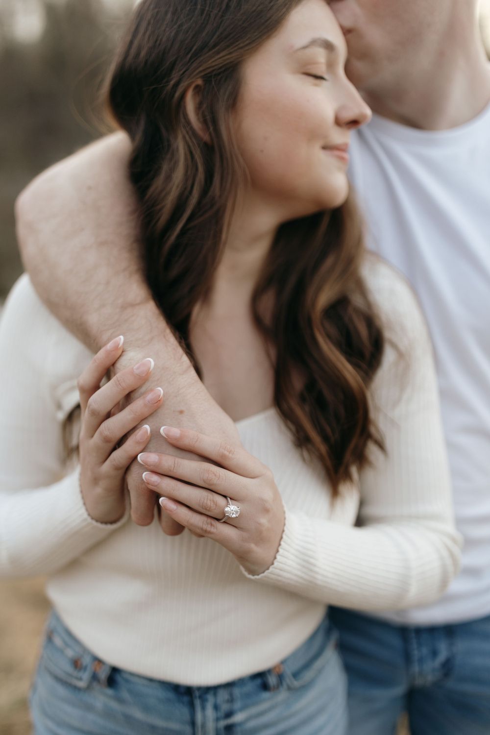 Close up of couple embracing while showing off engagement ring on her hand.
