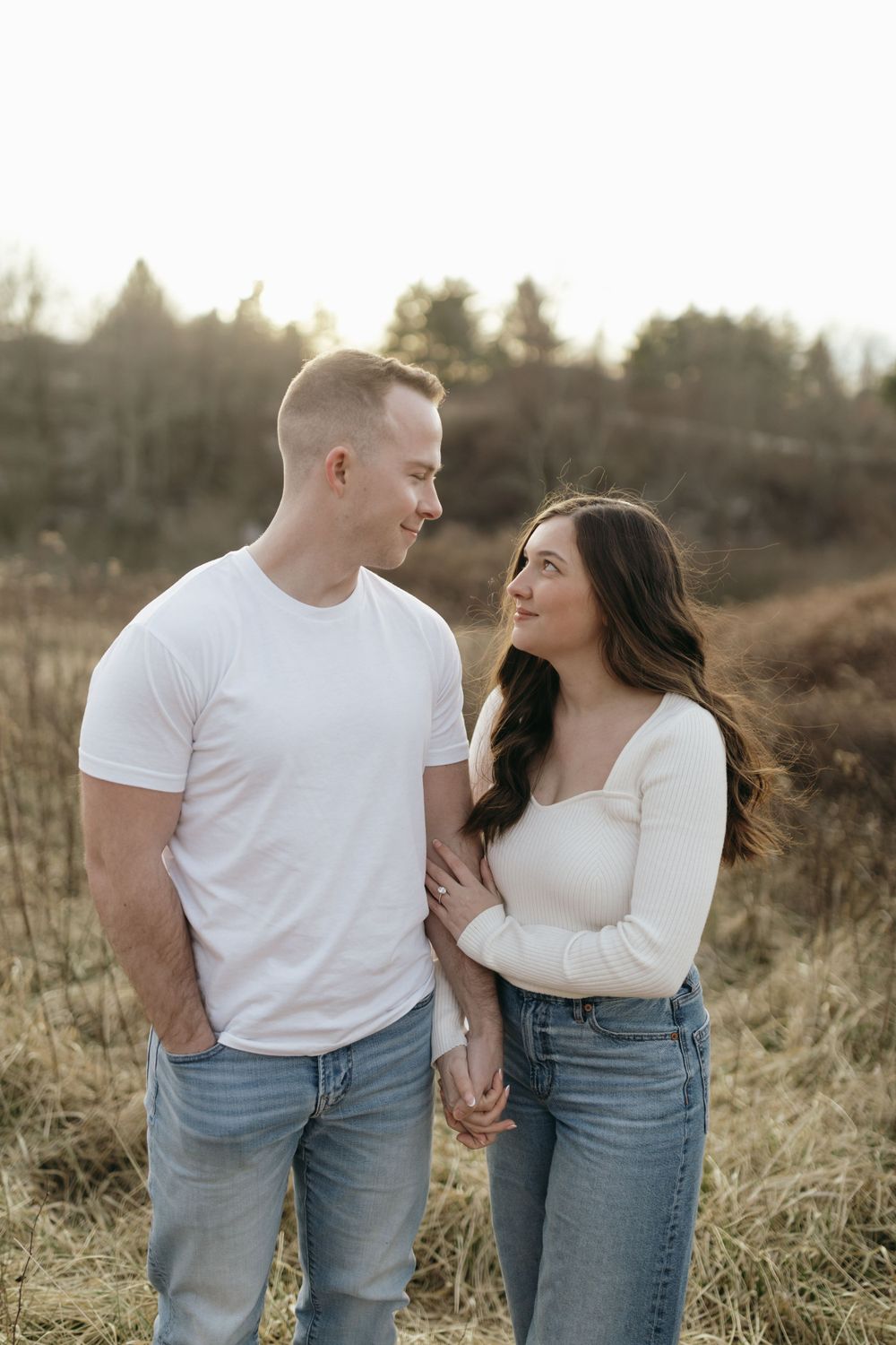 Affectionate couple in matching casual outfits pose together in golden field at sunset.