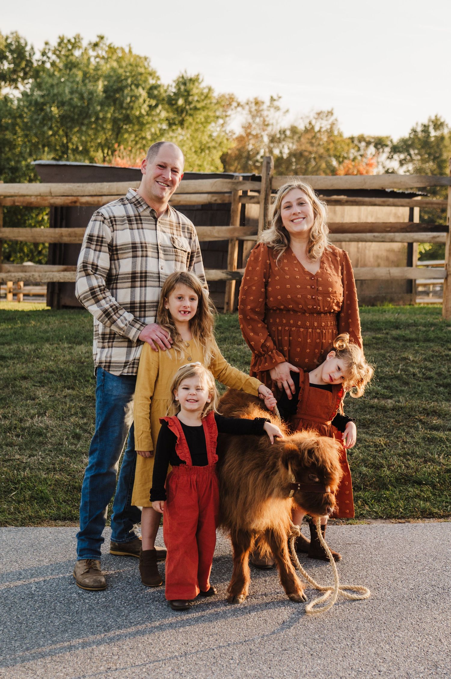 A family and their Highland cow pose together on a farm path during golden hour.