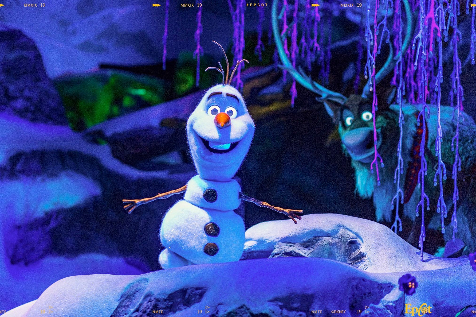 Olaf from Disney's Frozen movie appears in various poses against a snowy blue-lit backdrop during a theme park attraction.