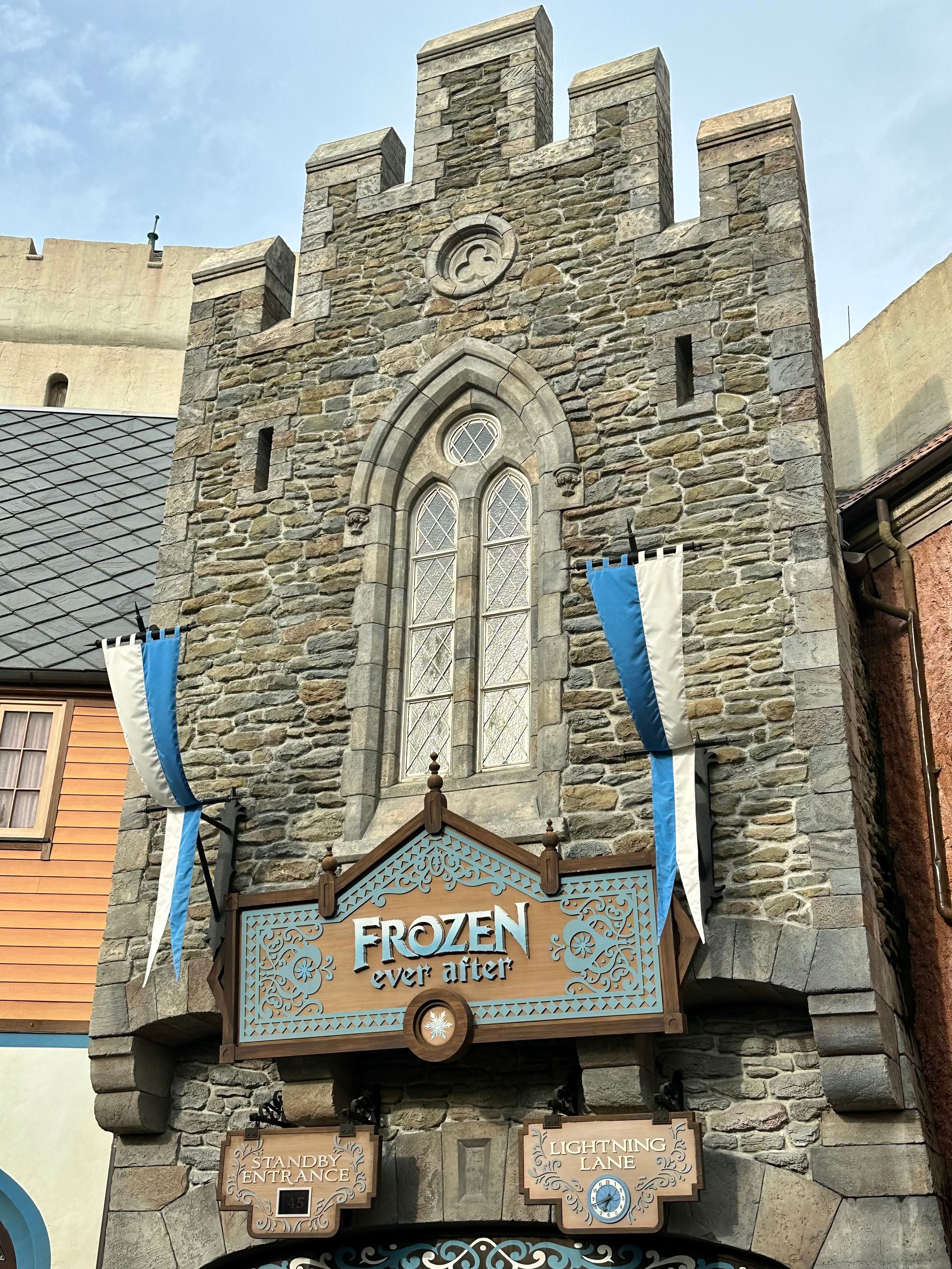 Stone facade of Disney's Frozen attraction entrance with Gothic architecture and blue banners at a theme park.