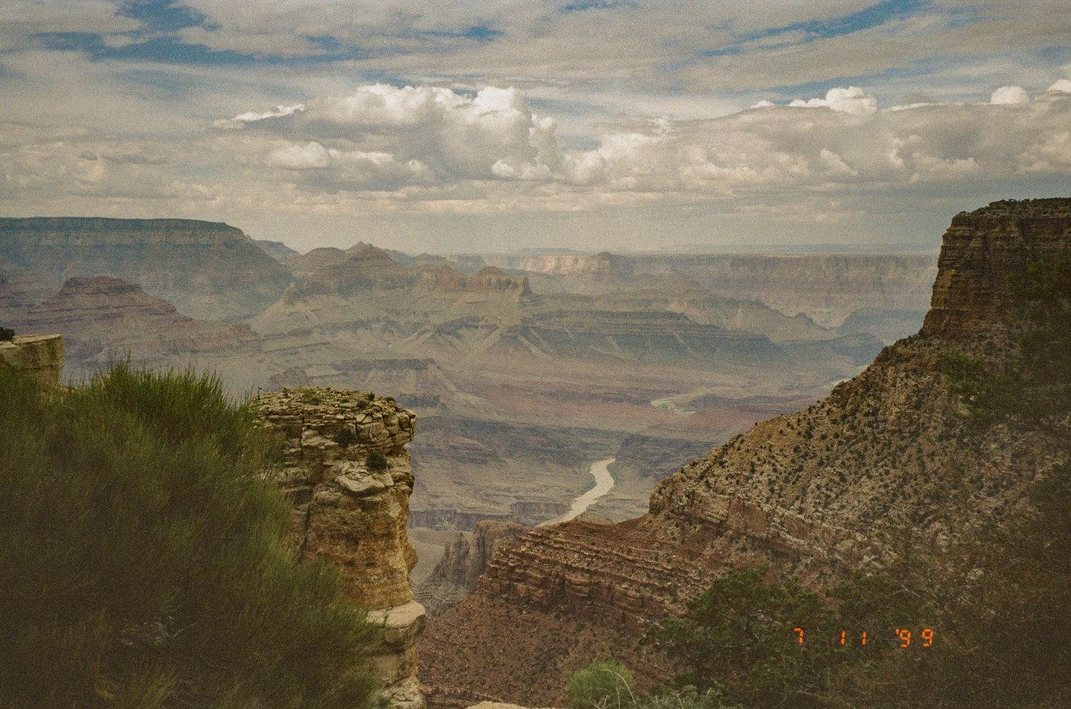 Sunlit view of Grand Canyon's layered cliffs and distant plateaus under dramatic clouds.