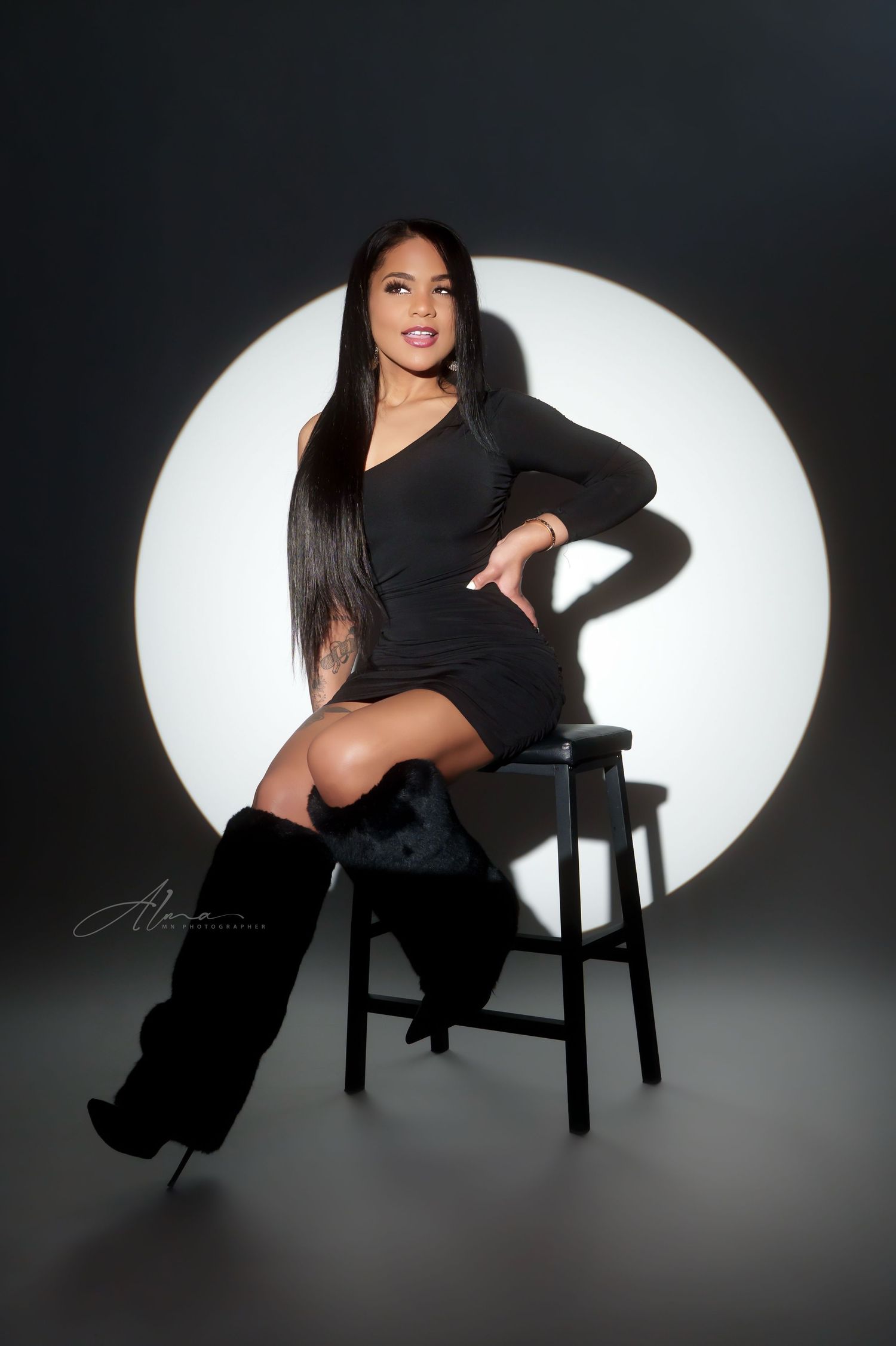 Fashion portrait on stool against circular white backdrop with dramatic lighting.