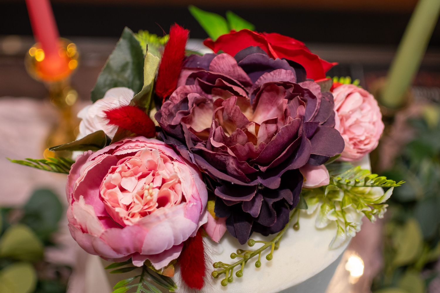 Pink and deep purple peony flowers arranged with green foliage in a decorative wedding centerpiece.