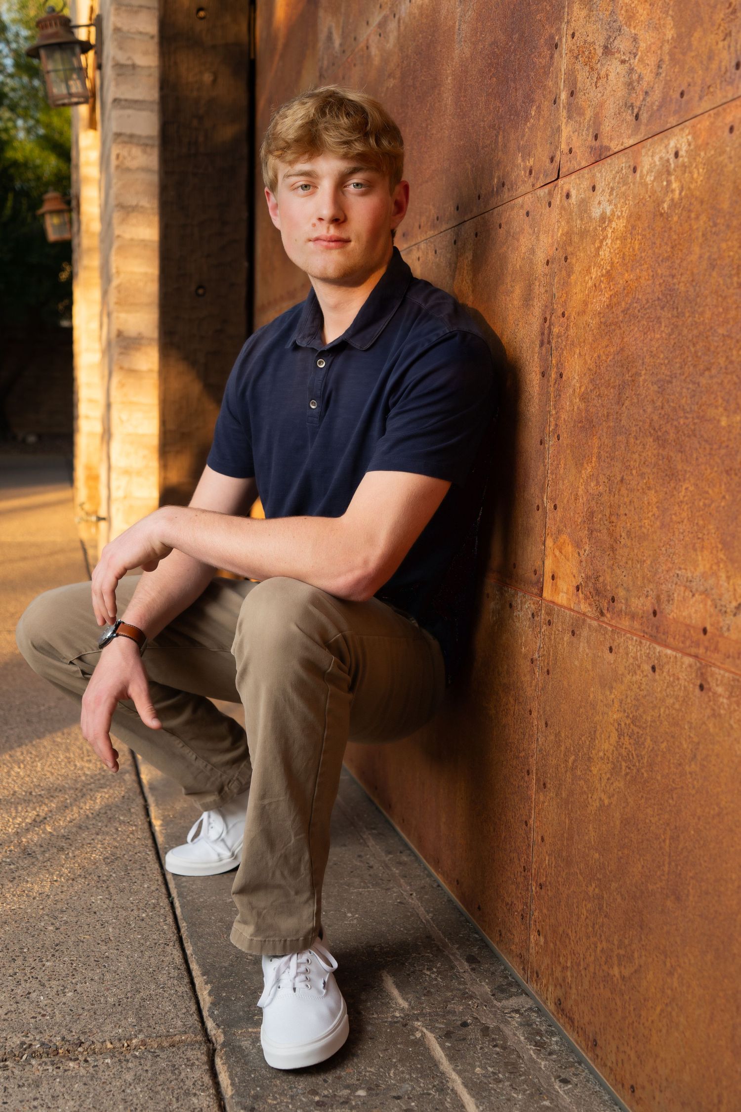 Casual portrait against rustic metal wall with warm lighting and urban backdrop.